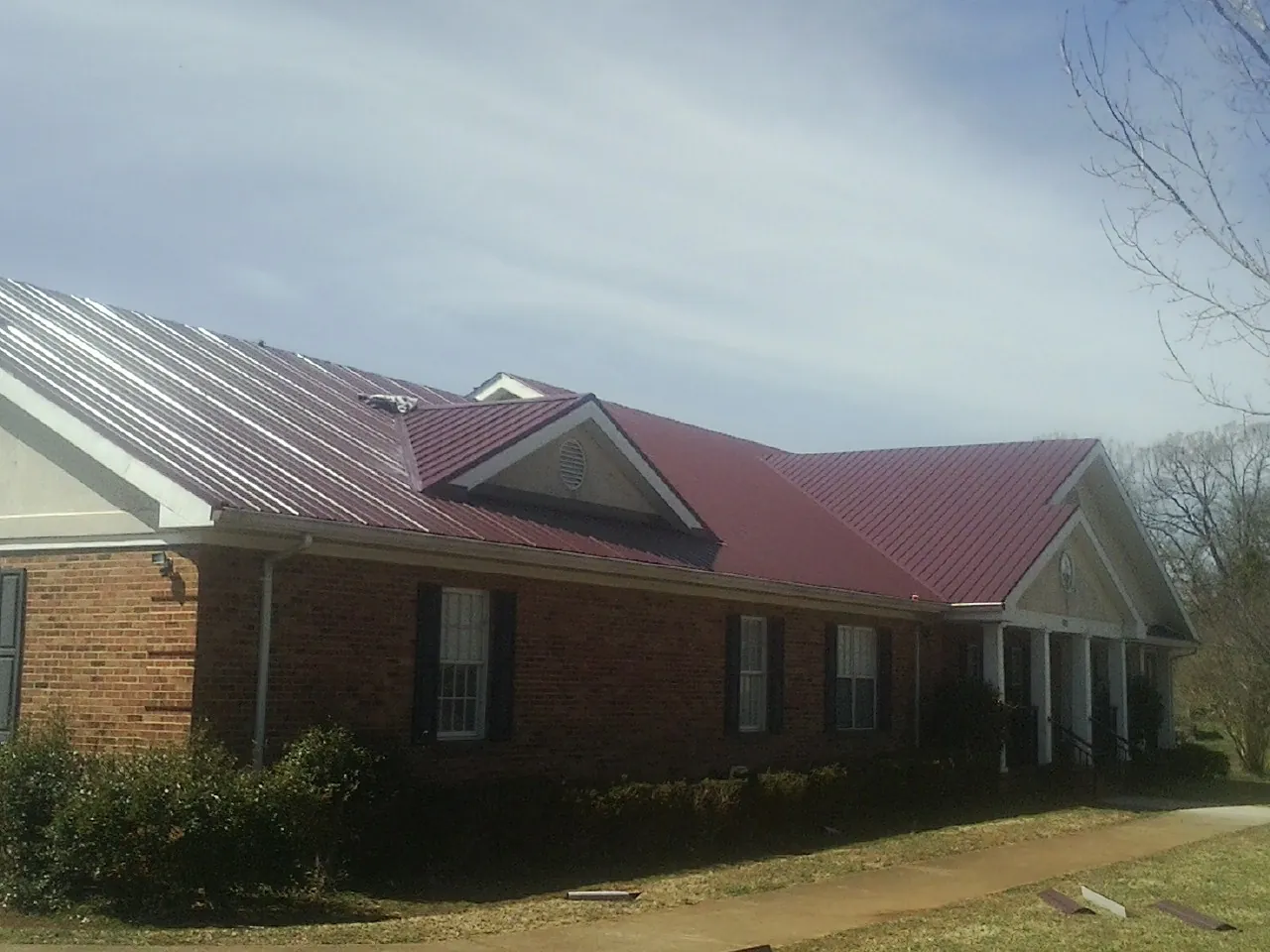 Red metal roof with gabled entries on a long brick building, from a Hail Damage Roof Repair job in Little River Academy