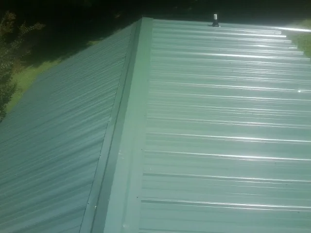 New green metal panels meeting at the ridge of a roof — Flat Roof Repair work by our crew in Little River Academy