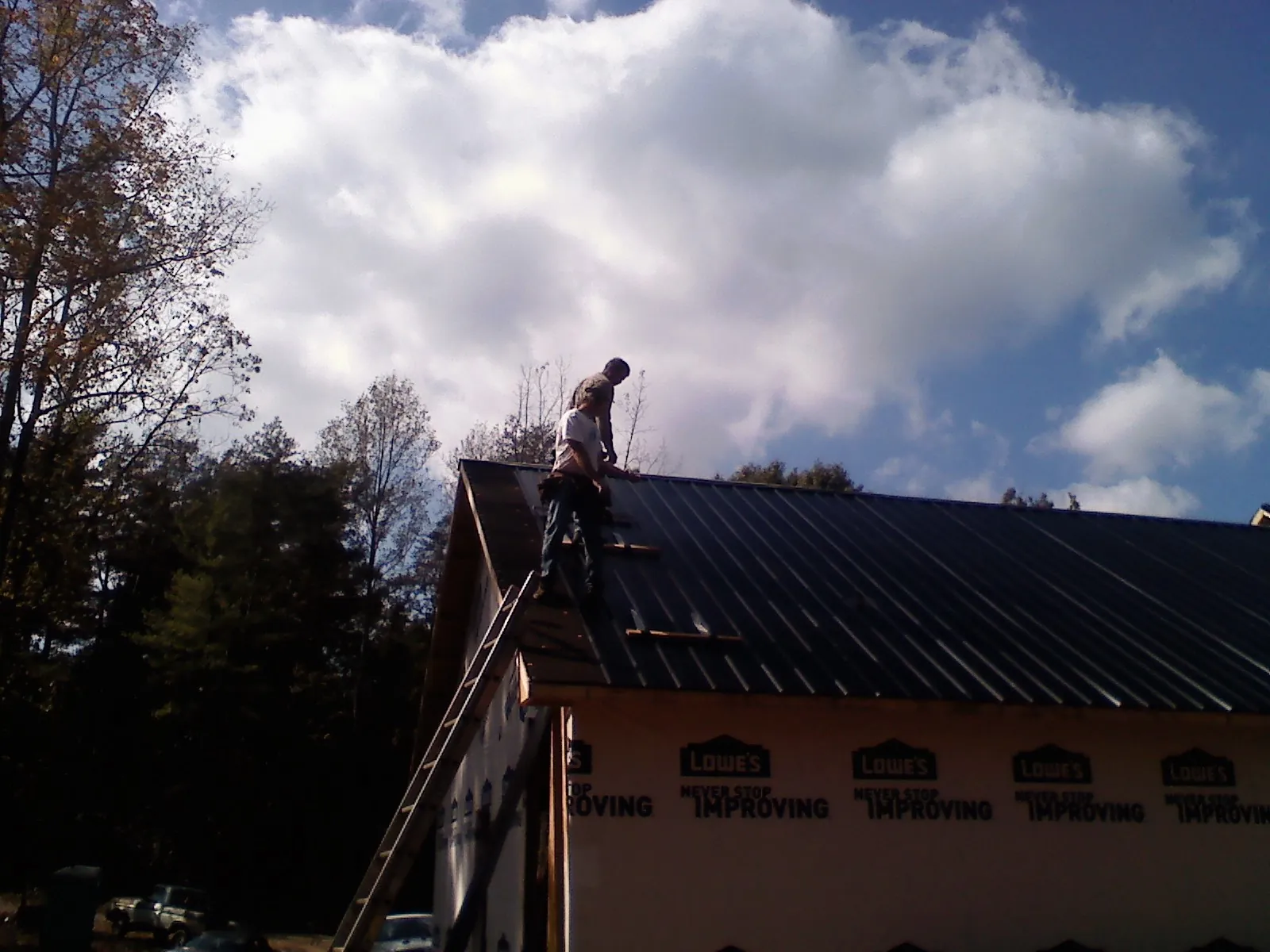 Roofer fastening dark metal panels high against a cloudy sky, from a Roof Inspection job in Little River Academy