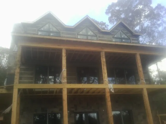 Dormers and porch framing on a large log home under construction — Roof Coating work by our crew in Little River Academy