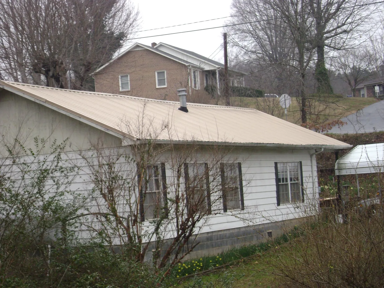 Tan metal roof on a white sided house set into a hillside — Commercial Roofing by Roofing Brothers in Little River Academy