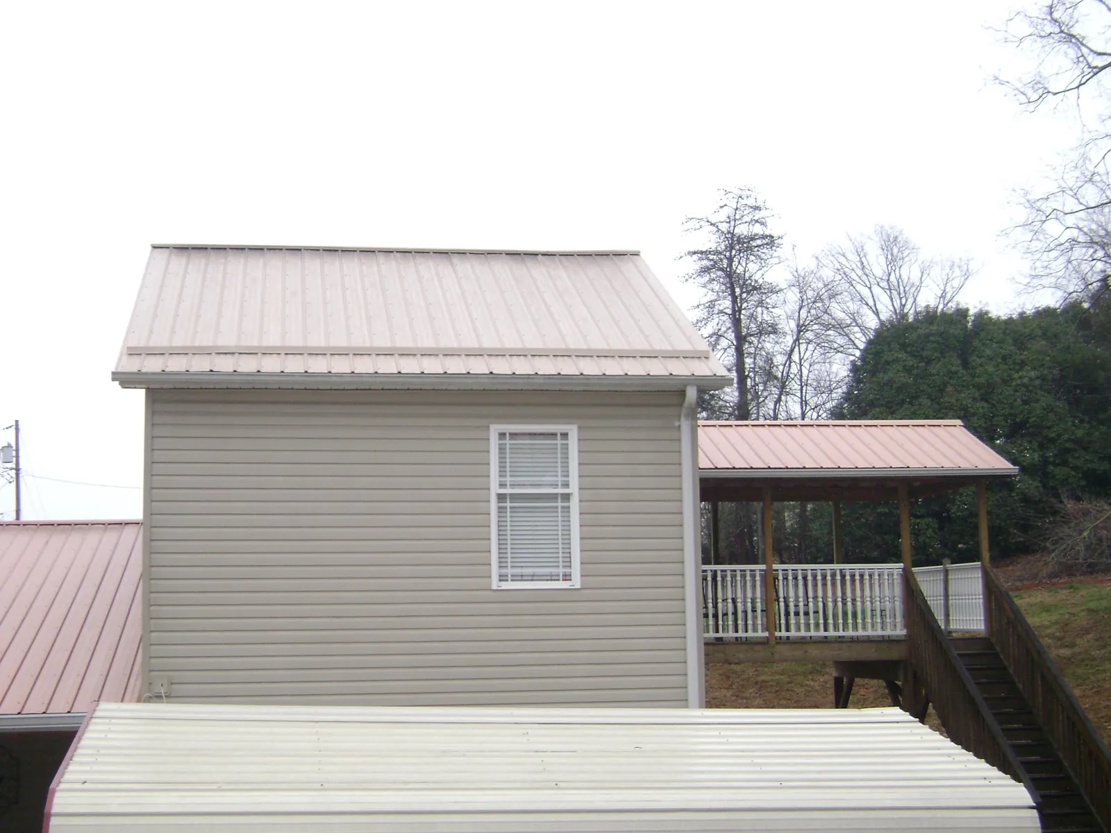 Tan metal roofs on a two story addition and attached porch, from a Roof Replacement job in Little River Academy